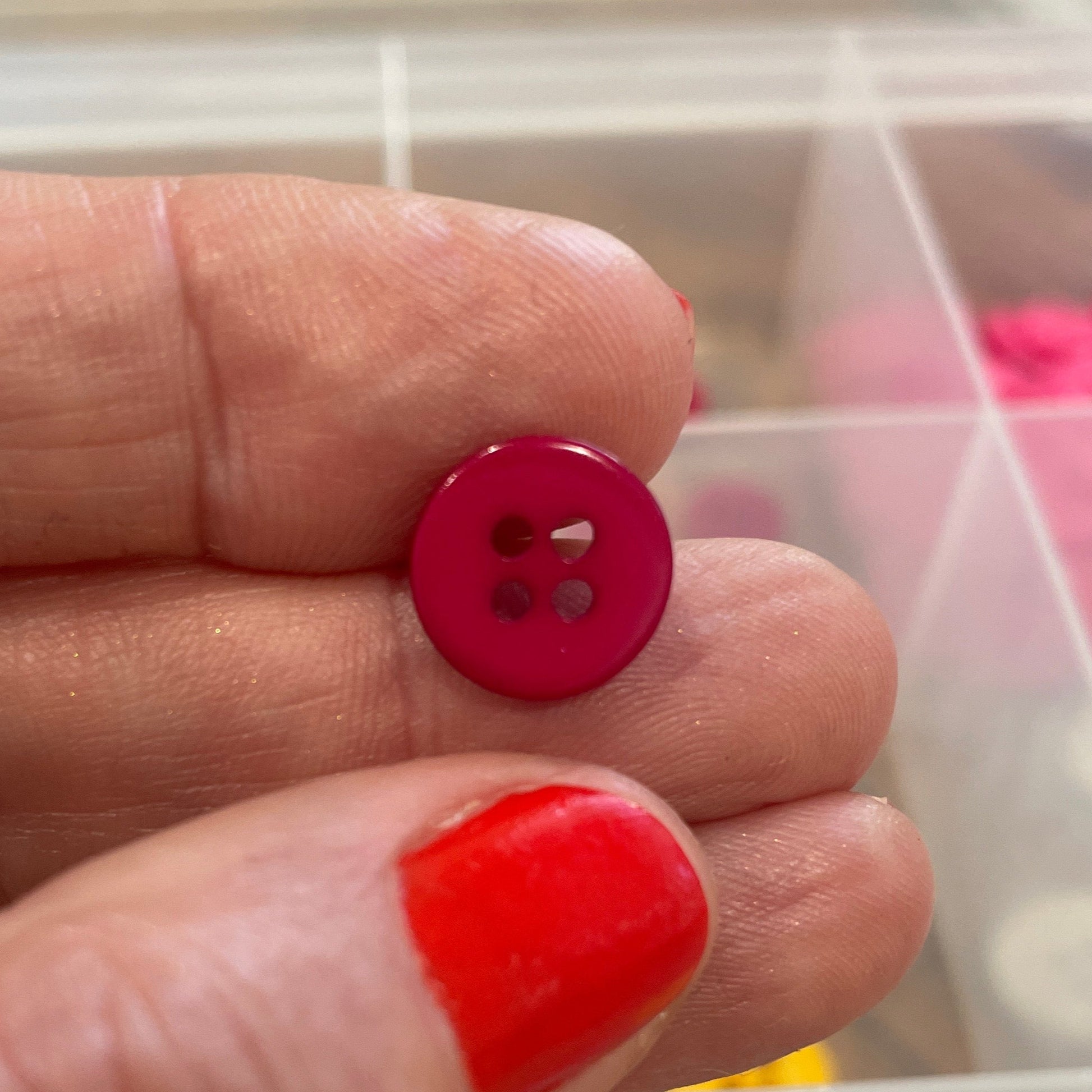 Hand holding two small buttons with a container of colorful buttons in the background
