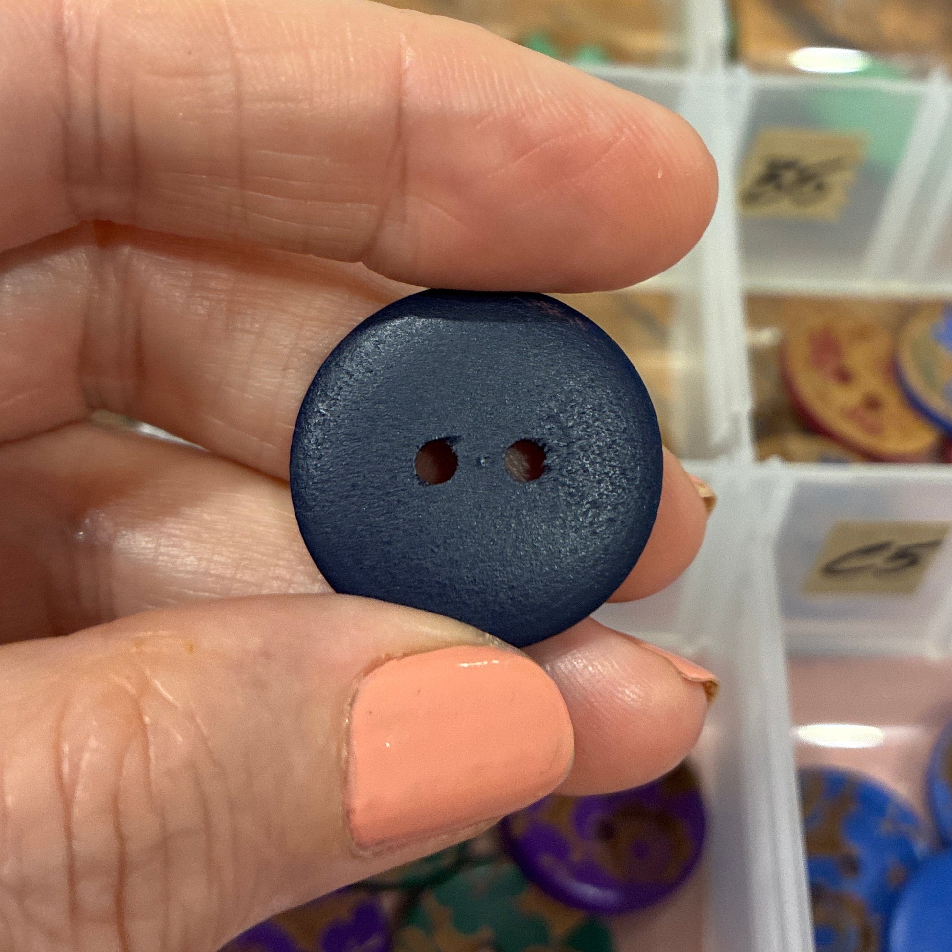 Black button held between fingers with a container of buttons in the background