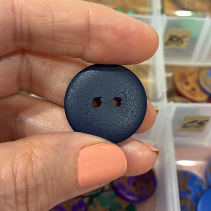 Black button held between fingers with a container of buttons in the background