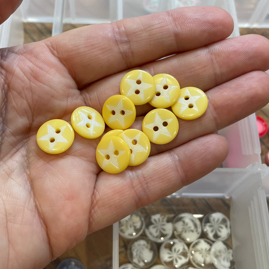 Hand holding yellow buttons with a container of buttons in the background