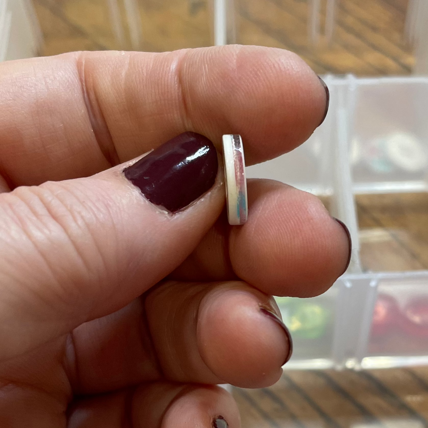 Hand holding a small button with a container of buttons in the background