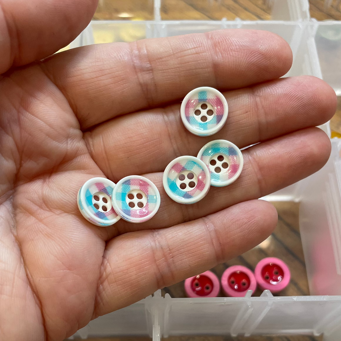 Hand holding colorful buttons with a container of similar buttons in the background