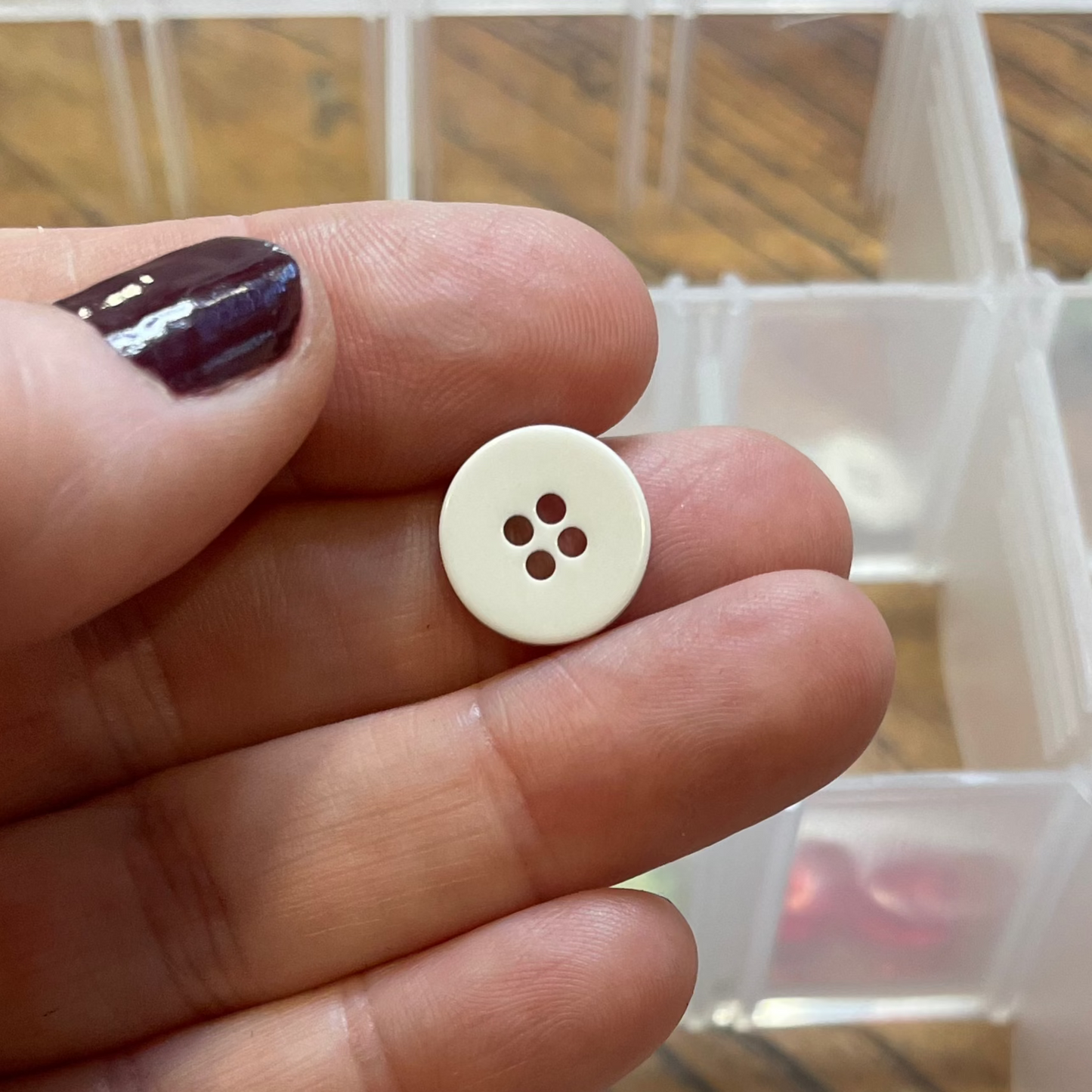 Hand holding a button with a container of various buttons in the background