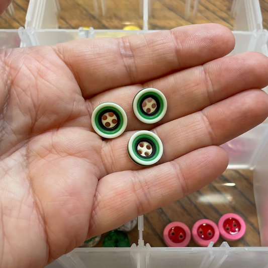 Hand holding three green buttons with a clear container of buttons in the background