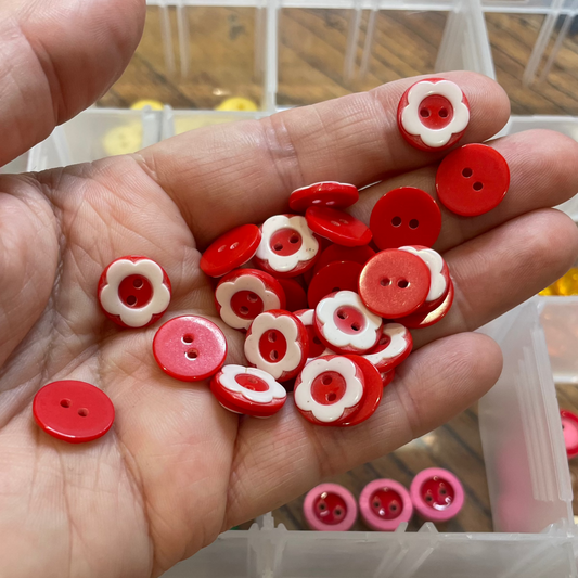 Hand holding red and white buttons with a clear container of buttons in the background.