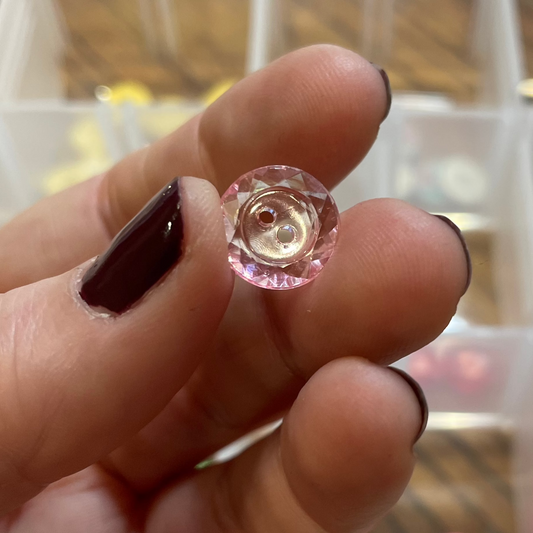 Hand holding a pink button with a clear container of buttons in the background