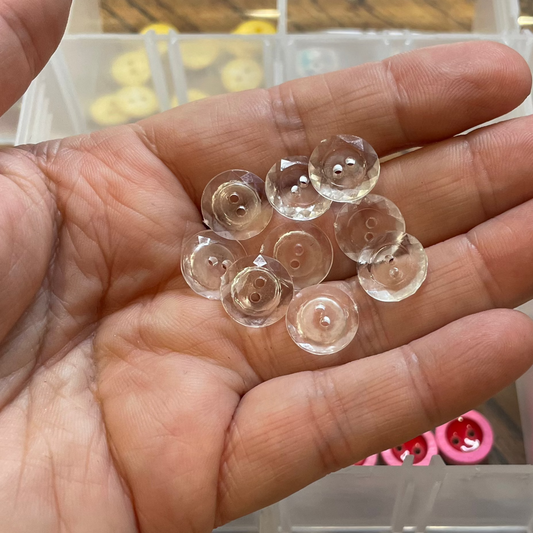 Hand holding clear buttons with a container of buttons in the background