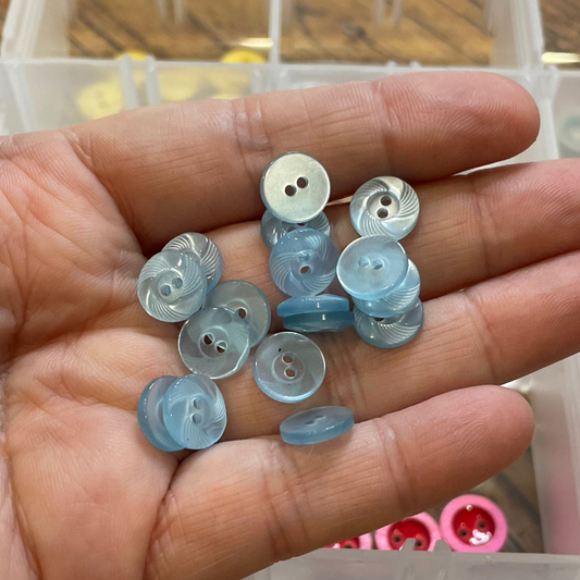 Hand holding small blue buttons with a clear container of buttons in the background
