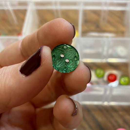 Hand holding a green button with a blurred background of a button organizer.