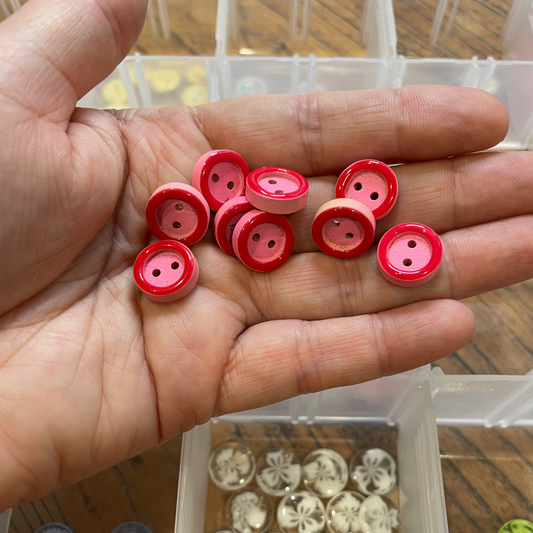 Hand holding red buttons with a clear container of buttons in the background