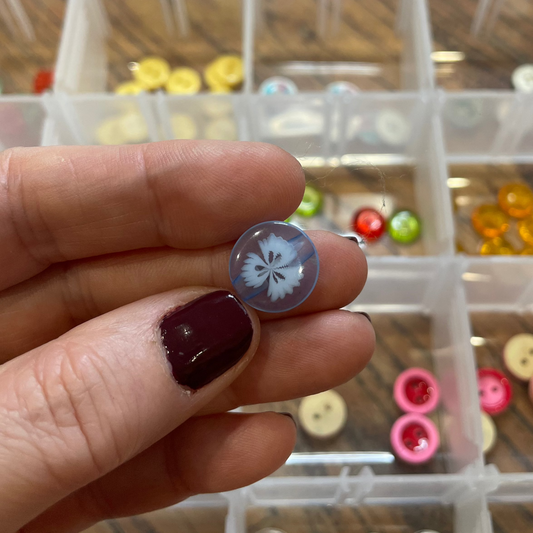 Close-up of a hand holding a button with a decorative center, blurred background of a button collection.