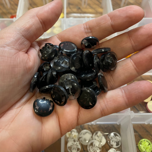 Hand holding black buttons with a blurred background of a container and items.
