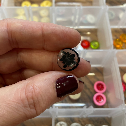 Hand holding a small button with a clear container of buttons in the background