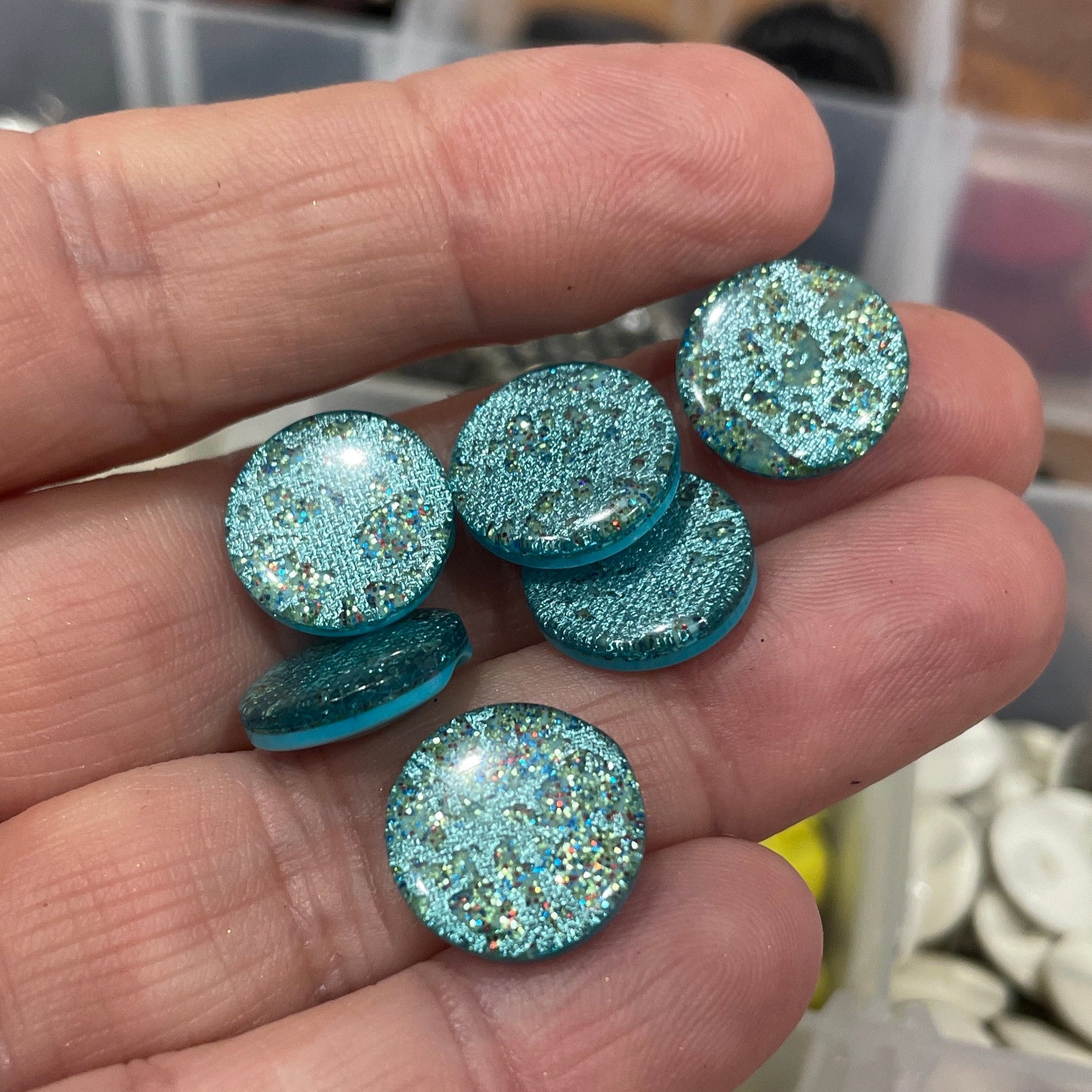 Hand holding blue glittery buttons with a blurred background of button containers.
