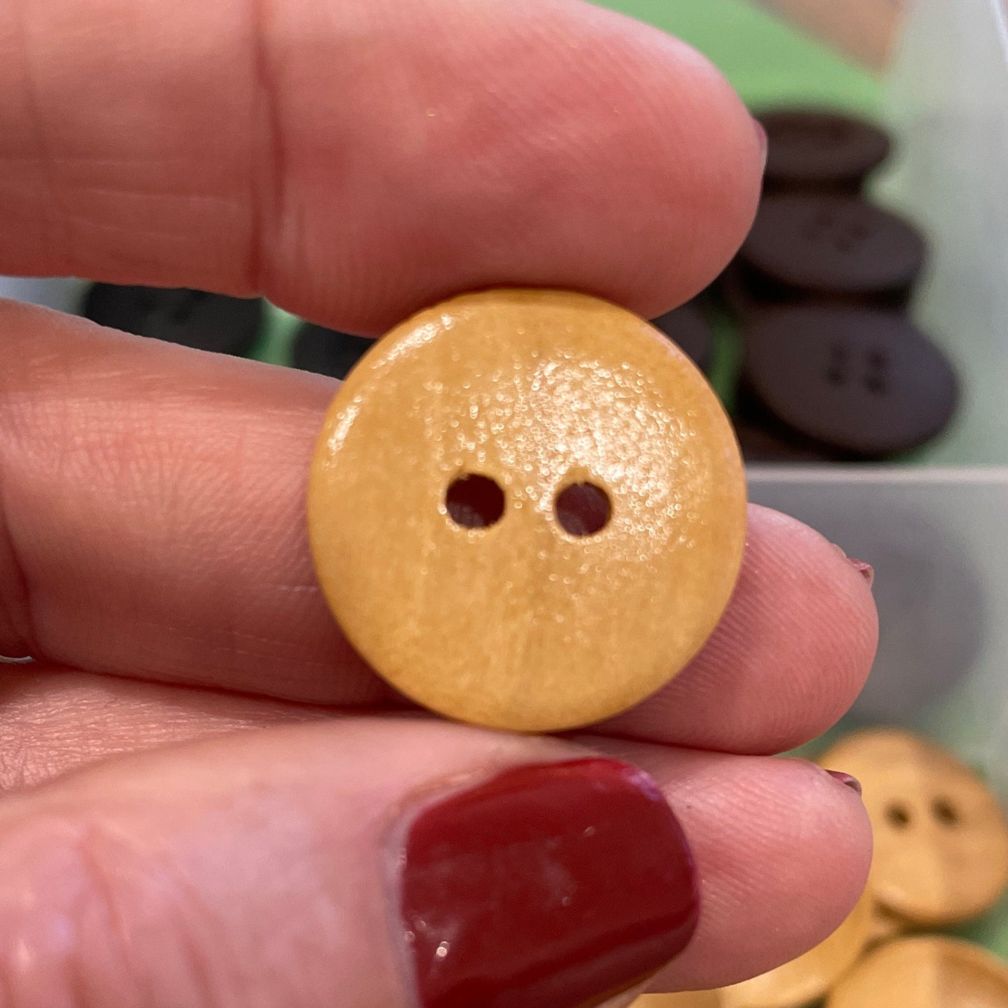 Hand holding a gold button with a container of buttons in the background