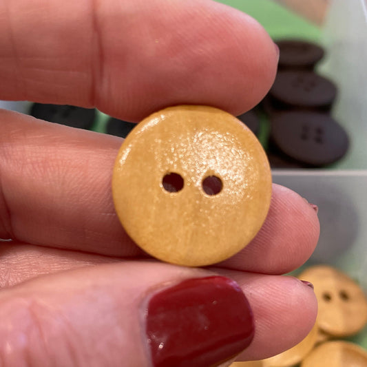 Hand holding a gold button with a container of buttons in the background