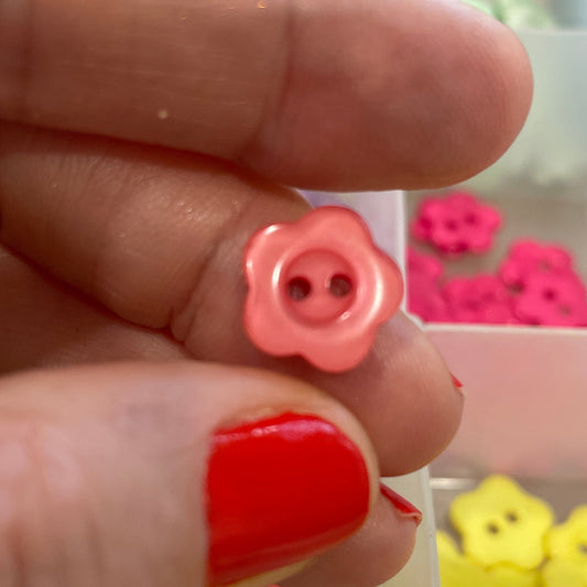 Hand holding a pink button with a container of colorful buttons in the background