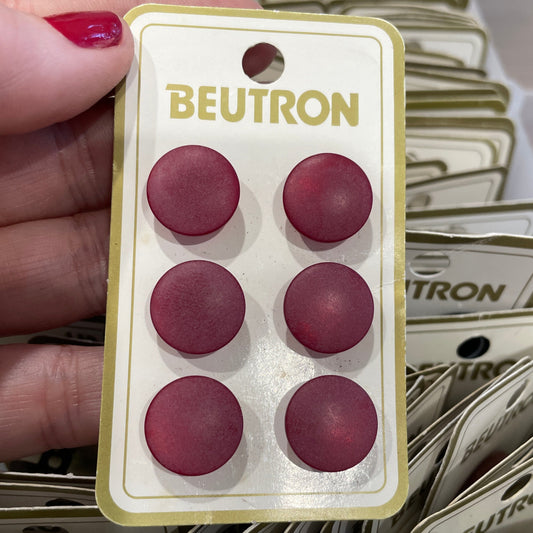 Hand holding a package of red buttons labeled 'Beutron' with more packages in the background.