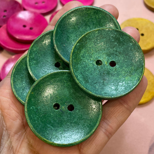 Hand holding green buttons with a pink and gold button background