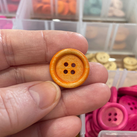 Hand holding a yellow button with a clear container of buttons in the background