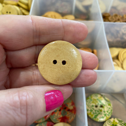 Hand holding a yellow button with a clear container of buttons in the background