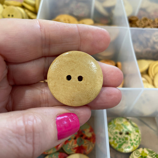 Hand holding a yellow button with a clear container of buttons in the background