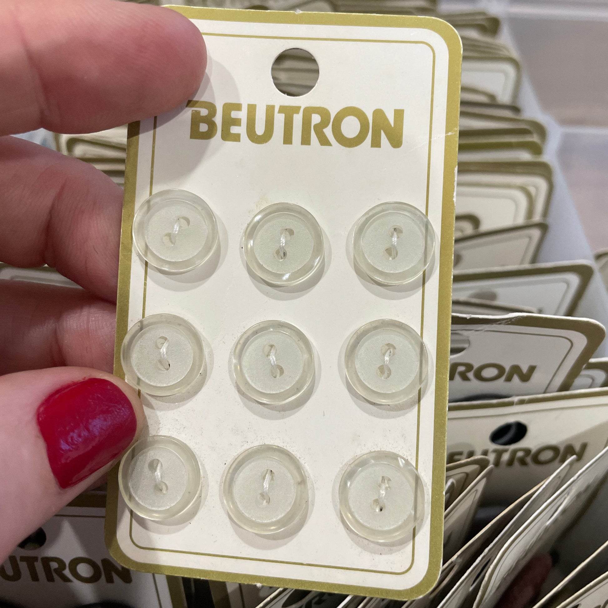 Packaged buttons with 'Beutron' branding held by a hand.