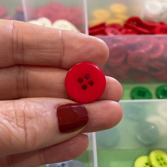 Hand holding a red button with a container of assorted buttons in the background