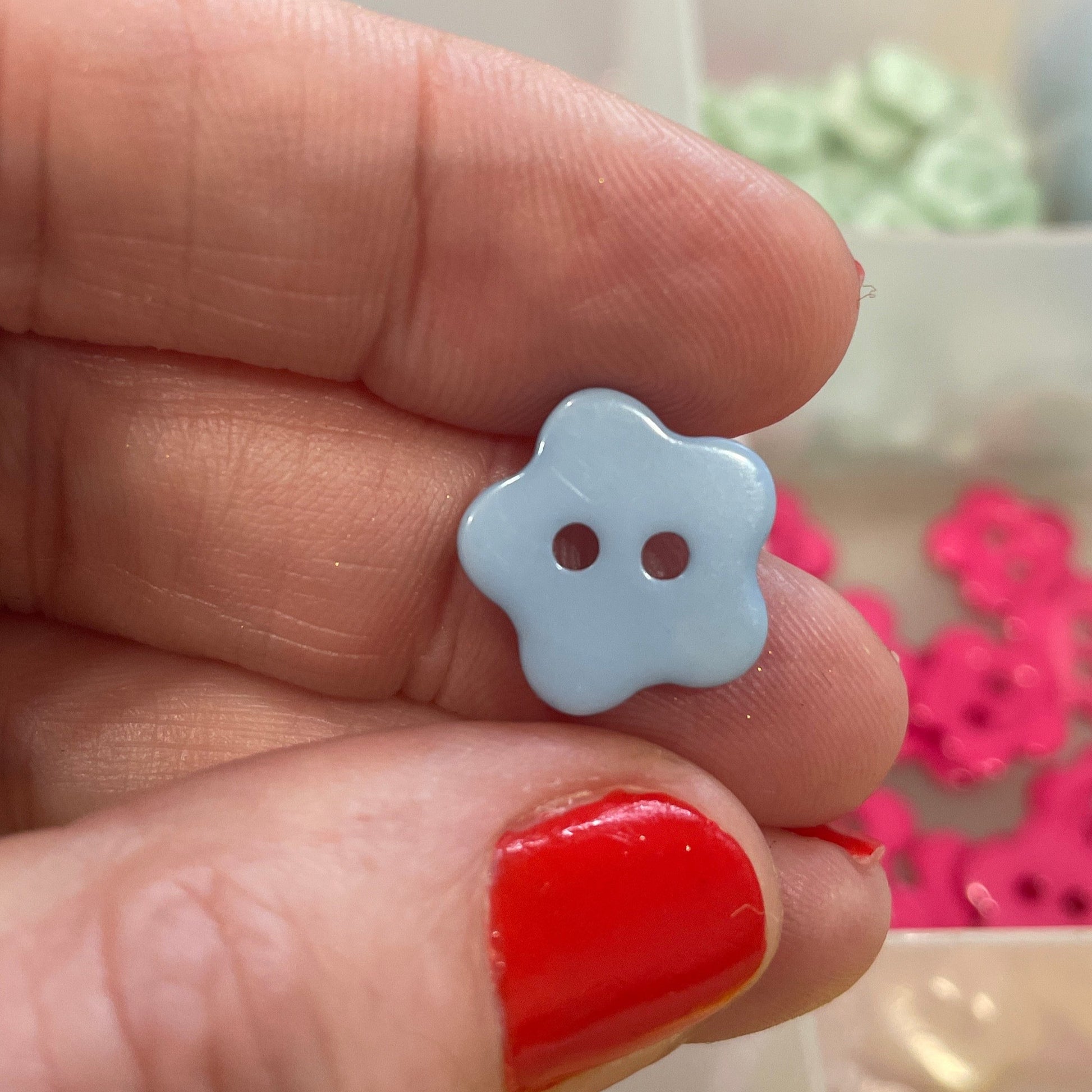 Hand holding a white flower-shaped button with a blurred background of colorful buttons.