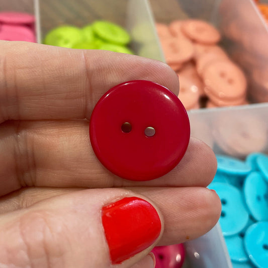 Hand holding a red button with a blurred background of colorful buttons