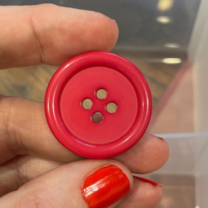 Hand holding a red button with a clear container of buttons in the background