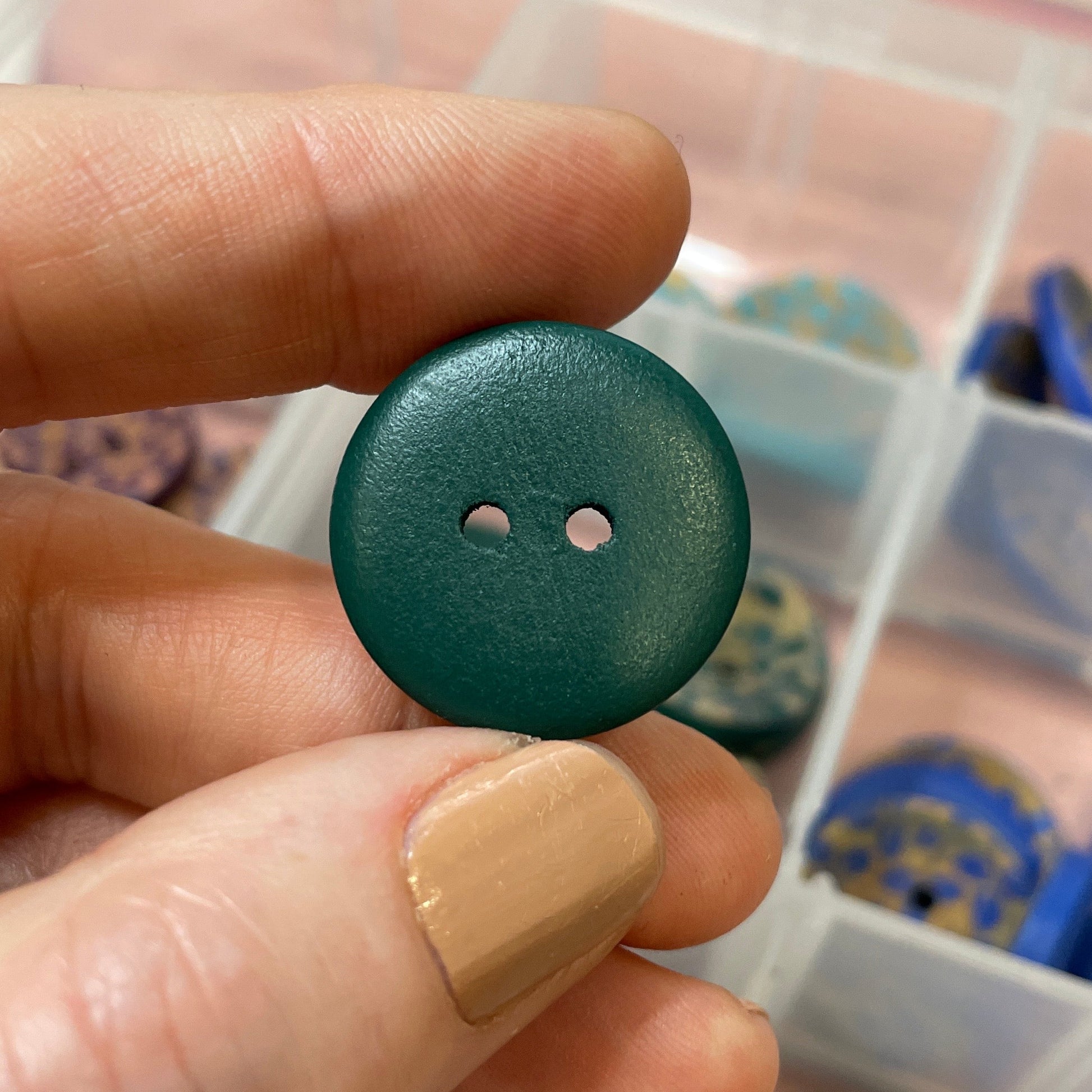 Green button held by a hand with a container of buttons in the background