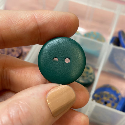 Green button held by a hand with a container of buttons in the background