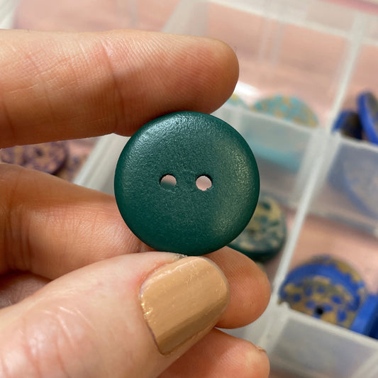 Green button held by a hand with a container of buttons in the background