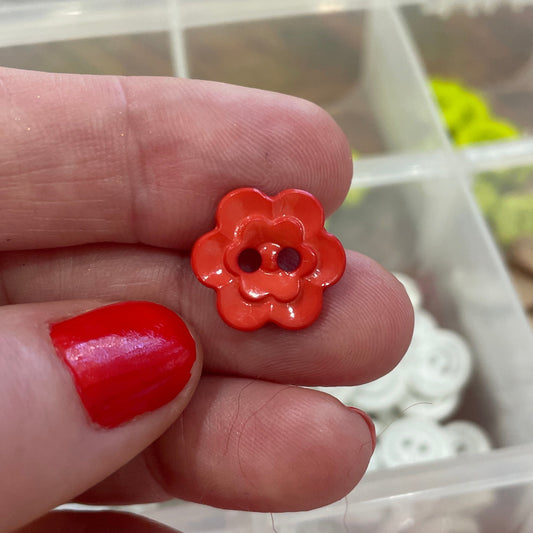 Hand holding a red flower-shaped button with a blurred background of button assortment.
