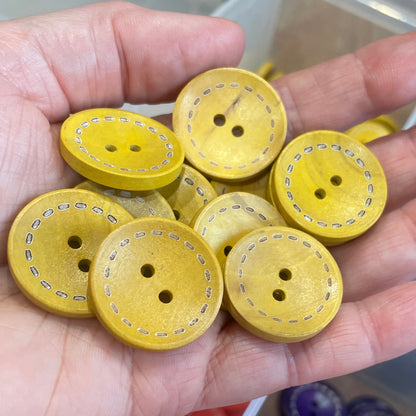 Hand holding yellow buttons with a container of assorted buttons in the background