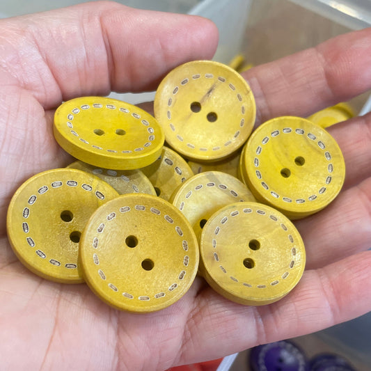 Hand holding yellow buttons with a container of assorted buttons in the background