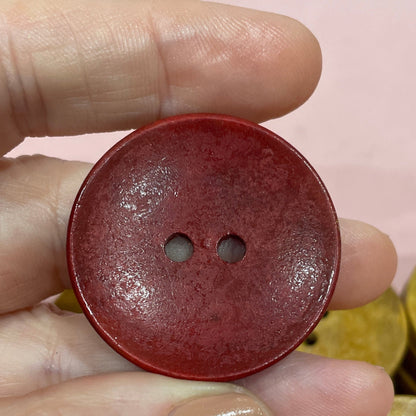 Hand holding a red button with other buttons on a pink surface