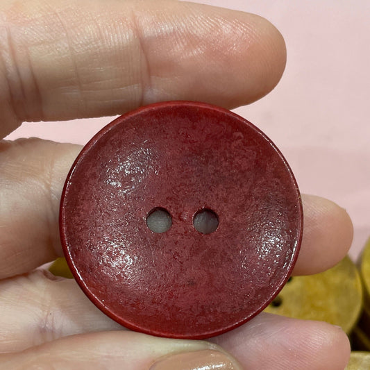Hand holding a red button with other buttons on a pink surface