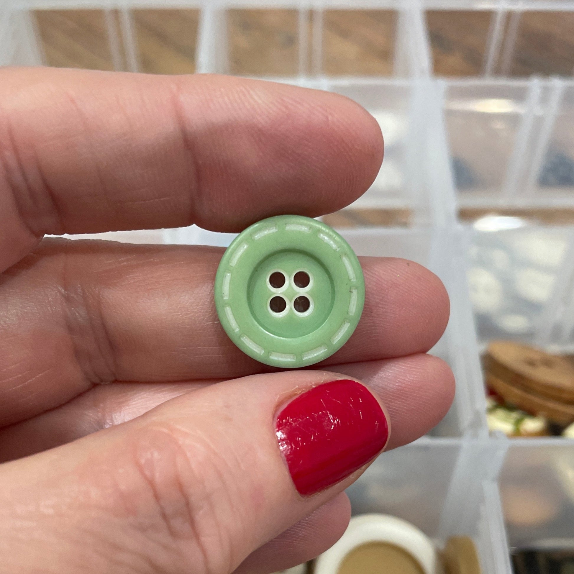Hand holding a green button with a container of buttons in the background