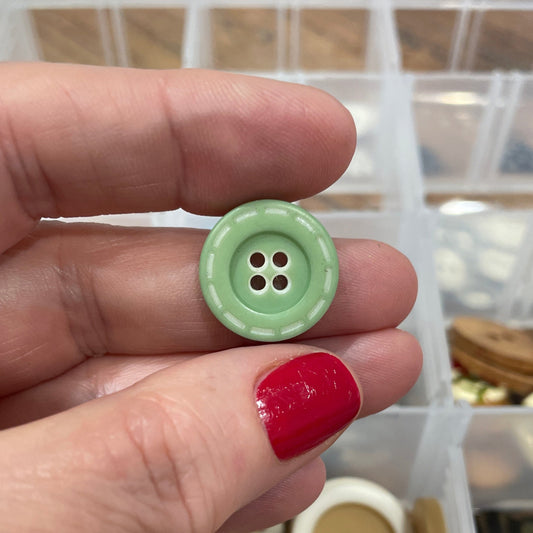 Hand holding a green button with a container of buttons in the background