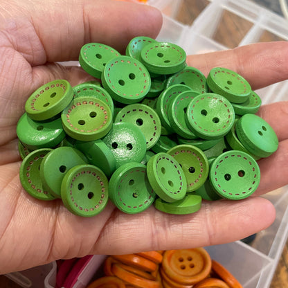 Hand holding green buttons with a container of orange buttons in the background.