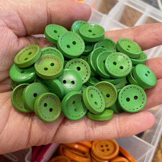 Hand holding green buttons with a container of orange buttons in the background.
