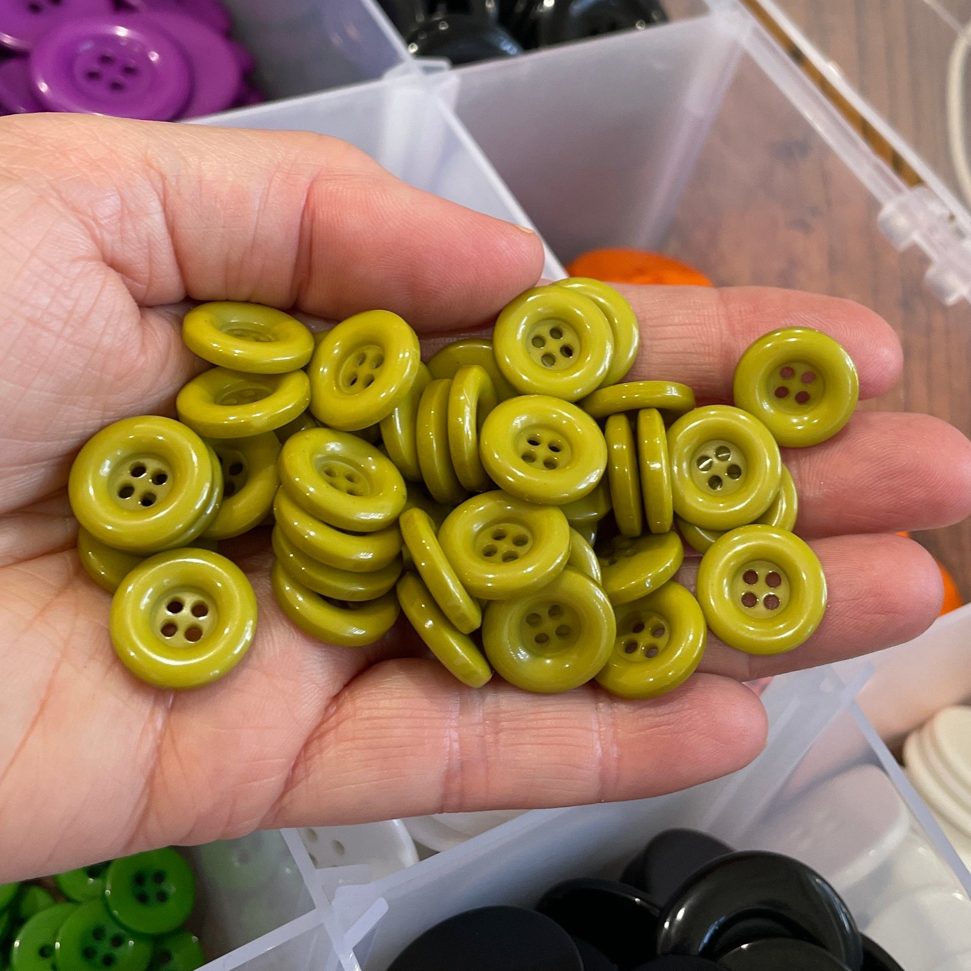 Hand holding a collection of yellow buttons with a container of assorted buttons in the background.