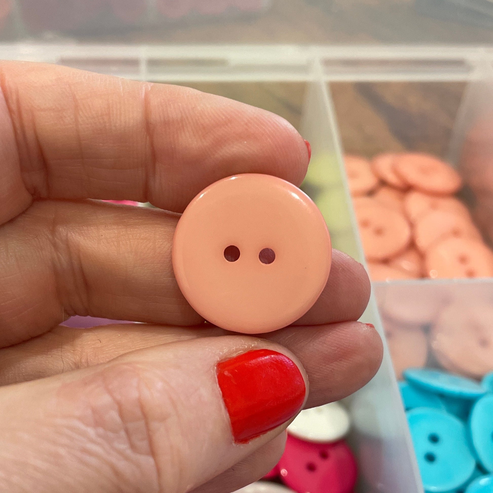 Hand holding a pink button with a background of colorful buttons in a container.
