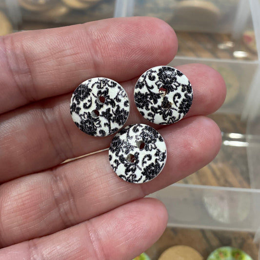 Hand holding three black and white patterned buttons with a container of buttons in the background.