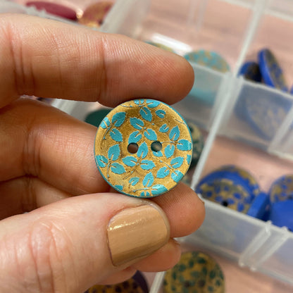 Person holding a gold and blue button with a container of buttons in the background