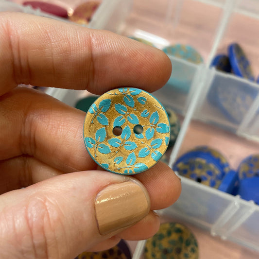 Person holding a gold and blue button with a container of buttons in the background