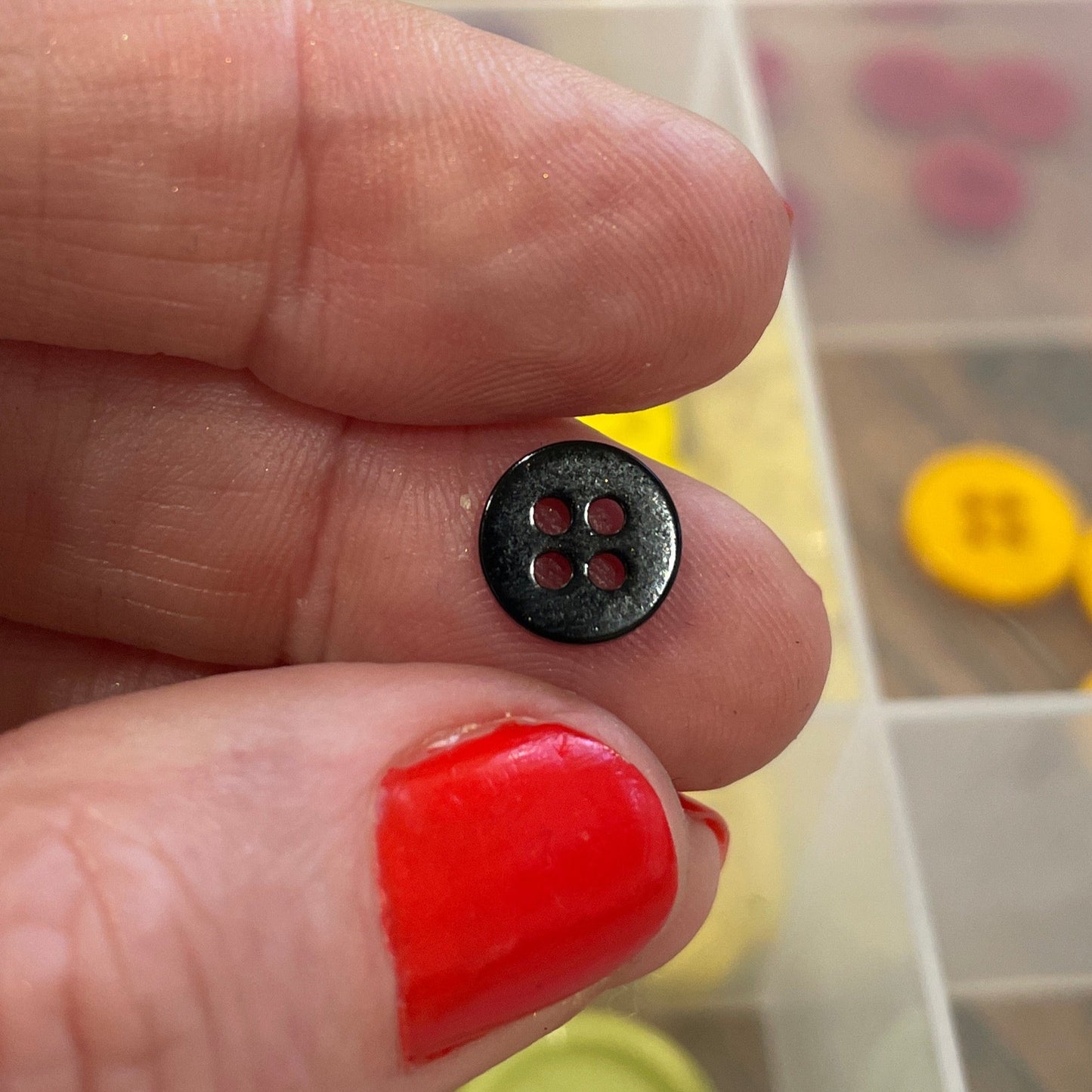 Hand holding a black button with a blurred background of colorful buttons in a container
