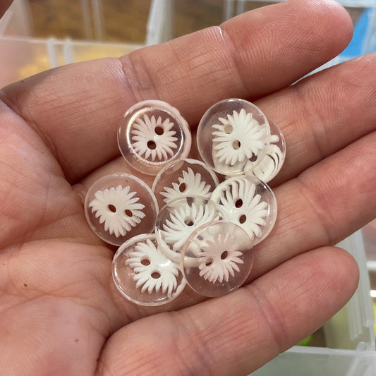 Hand holding small decorative gears with a container of similar items in the background.